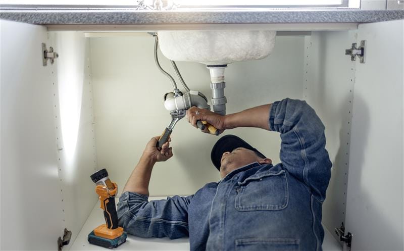 Plumber repairing pipes beneath a bathroom sink in Woodland